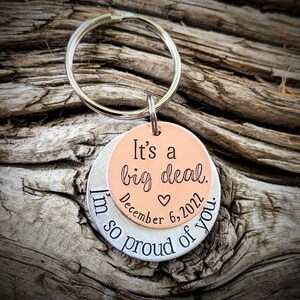 Puede incluir: Un llavero de plata y cobre con el texto "It's a big deal. December 6, 2022. I'm so proud of you."