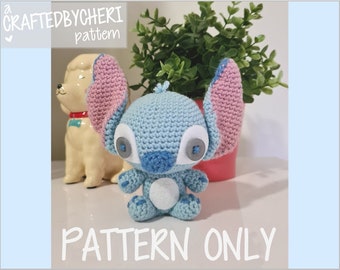 May include: A blue and pink crocheted Stitch character with large eyes and a white belly. The character is sitting on a table with a potted plant and a ceramic dog figurine behind it. The text "CRAFTEDBYCHERI pattern" is at the top of the image and "PATTERN ONLY" is at the bottom of the image.