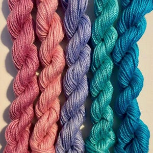 May include: Five skeins of colourful yarn in shades of pink, purple, and teal. The yarn is tightly twisted, creating a textured appearance. The colours range from light to dark, offering a gradient effect. Ideal for knitting or crochet projects.