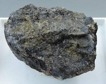 May include: A dark gray rock with green and black mineral inclusions. The rock has a rough, uneven surface.