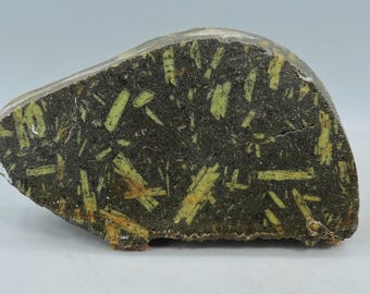 May include: A rough-hewn, irregularly shaped stone with a dark gray base color. The stone is heavily speckled with light green, elongated crystal formations. The overall appearance suggests a natural, geological specimen.