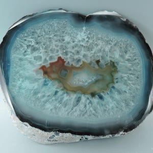 May include: A slice of agate with a blue, green, and brown banded pattern. The agate is translucent and has a crystalline texture.