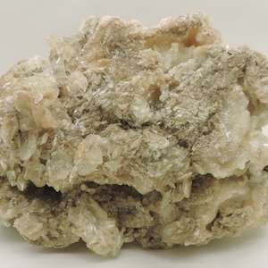 May include: A large, rough, light brown rock with clusters of white, translucent crystals. The crystals are arranged in a layered pattern, creating a unique and interesting texture.