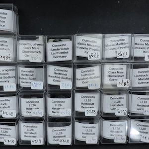May include: A collection of small, clear plastic boxes containing various mineral specimens. Each box has a label identifying the mineral, its location, and a number. The minerals include Connelite, Oliveni, Sandersloch, and more.