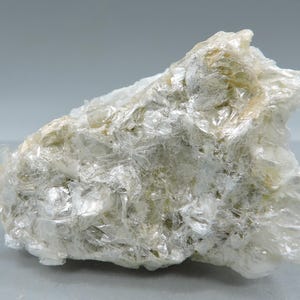 May include: A close-up of a mineral specimen, displaying a layered, translucent structure. The rock formation has a pale, off-white colour with subtle hints of yellow and green. The texture appears crystalline and flaky, with light reflecting off the surfaces.