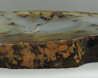 Op de afbeelding: Een grote, natuurlijke agaat geode kom met een lichtgrijze binnenkant en bruine, witte en zwarte banden aan de buitenkant. De kom is onregelmatig gevormt en heeft een ruwe, natuurlijke textuur.