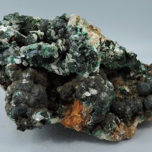 May include: A cluster of green malachite and white calcite crystals on a dark grey matrix. The malachite is in botryoidal form, with rounded, grape-like clusters. The calcite is in sharp, well-defined crystals.