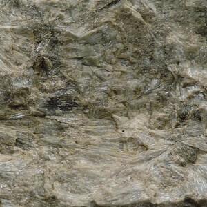 May include: Close-up of a textured rock formation with a mix of gray and light green hues. The surface has a layered appearance with crystalline structures and rough, uneven textures. The overall look is natural and earthy.