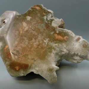 以下が含まれることがあります： オレンジと赤の模様のある、ざらざらとした灰色と茶色の岩。岩は不規則な形をしていて、表面はざらざらしている。