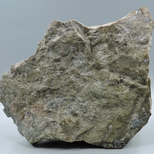 May include: A rough, irregularly shaped rock formation with a textured surface. The rock displays a mix of gray, green, and white hues, with visible crystalline structures. The overall appearance suggests a natural mineral specimen.