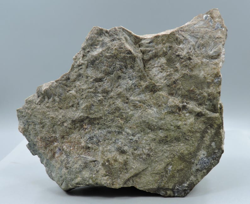 May include: A rough, irregularly shaped rock formation with a textured surface. The rock displays a mix of gray, green, and white hues, with visible crystalline structures. The overall appearance suggests a natural mineral specimen.