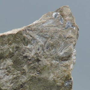 May include: Close-up of a rough, textured rock formation. The rock has a mix of gray and beige tones, with crystalline structures radiating outwards. The surface is uneven, with visible mineral deposits and a slightly weathered appearance.