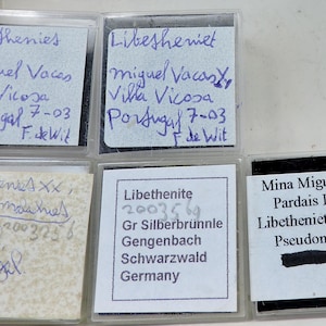 May include: A collection of labeled mineral samples in clear plastic cases. The handwritten labels include details such as the mineral name, location, and collector's name. The samples are from Portugal and Germany.