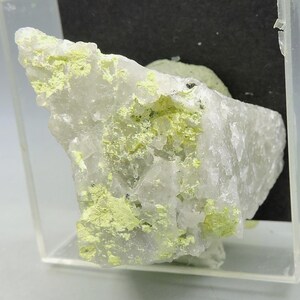 May include: A raw mineral specimen featuring a translucent white crystalline structure with patches of vibrant, pale yellow mineral deposits. The jagged, angular rock is displayed within a clear, square plastic protective case.