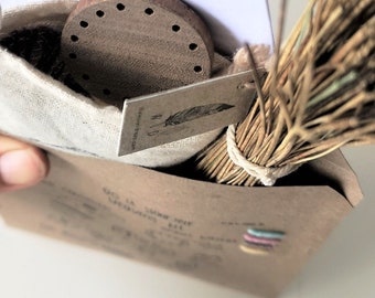 May include: A brown paper envelope with a white cloth bag inside. The bag contains a wooden circle with holes and a bundle of dried grass. The envelope has a label that says "Good Vibes Only".