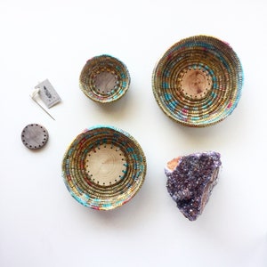 May include: Four woven baskets of different sizes with colourful accents, a small round wooden disc, and a large amethyst crystal.
