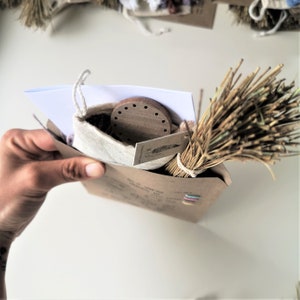 May include: A brown paper bag with a white cloth bag inside. The cloth bag contains a wooden round object with holes. A bundle of dried grass is on top of the bag. The bag has the text "Get it Together" printed on it.