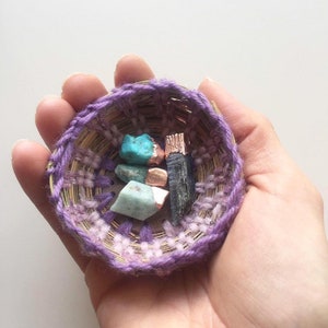 May include: A small purple woven basket containing a variety of colourful stones and metal accents.
