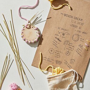 May include: A DIY weaving kit with a small brown basket, natural materials, yarn in pink and yellow, and instructions on a brown paper card. The card reads "The Woven Dream Do it yourself Weaving kit".