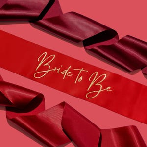 May include: Red and burgundy satin sashes with gold glitter lettering that reads "Bride To Be".