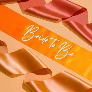 May include: Orange and peach satin sashes with the text "Bride to Be" written in white cursive.