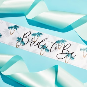 May include: White satin sash with a palm tree print and the text "Bride to Be" in black script.