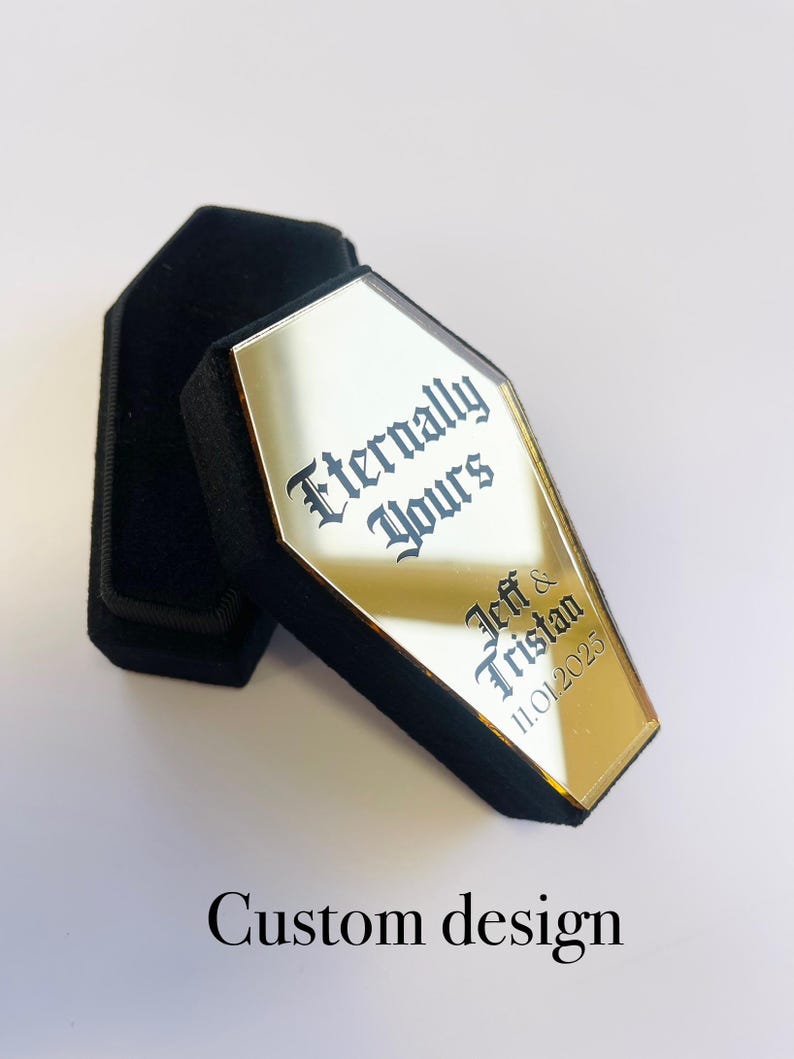 May include: Gold coffin-shaped box with a mirrored surface. The box has the text "Eternally Yours" and "Jeff & Tristan 11.01.2025" engraved on it.