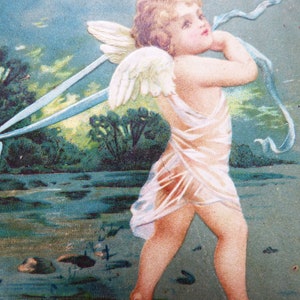 Op de afbeelding: Een vintage ansichtkaart met een cherubijn met vleugels, die een witte jurk draagt en een blauw lint vasthoudt. De engel staat in een landschap met een blauwe lucht en groene bomen.