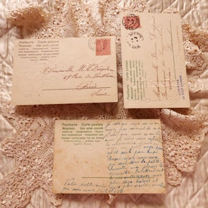 Op de afbeelding: Drie vintage ansichtkaarten met handgeschreven berichten in het Frans. De ansichtkaarten liggen op een kantonderlegger en hebben een cr&egrave;mekleurige achtergrond. De tekst op de ansichtkaarten luidt "Postkarte Carte postale" en "Mademoiselle M.R. Despedes 67 Rue de Freithin Paris".
