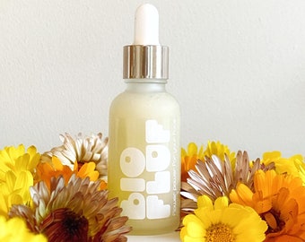 May include: A glass bottle of Bio Flor face serum with a white label that says "Bio Flor Flower Power for your face". The bottle is surrounded by yellow and orange flowers.