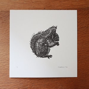 May include: Black and white linocut print of a squirrel sitting on its haunches, looking to the right. The print is signed "E. Williamson 2022" in the bottom right corner.