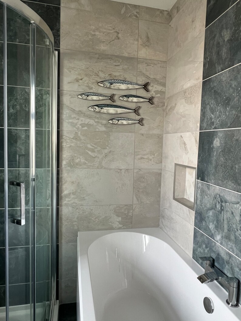 May include: A bathroom scene featuring a white bathtub, a glass shower enclosure, and a wall-mounted decorative fish sculpture. The fish are silver with black and blue details, arranged in a school-like formation on the tiled wall.