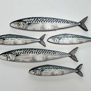 May include: Five wooden mackerel fish decorations. Each fish is painted with a silver body, black and blue markings, and a black tail. The fish are arranged in a group, with varying sizes and orientations.