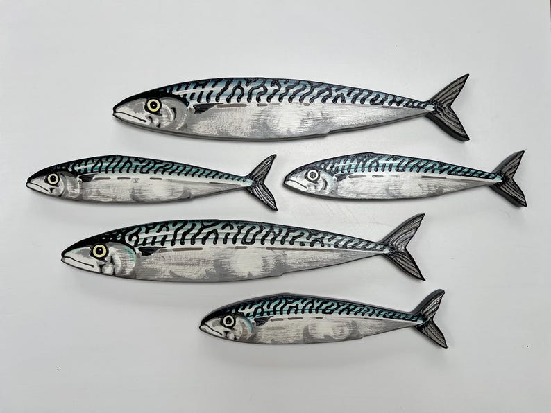 May include: Five wooden mackerel fish decorations. Each fish is painted with a silver body, black and blue markings, and a black tail. The fish are arranged in a group, with varying sizes and orientations.