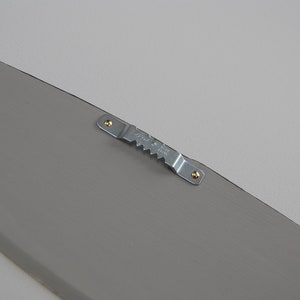 May include: A gray, wooden decorative piece with a metal sawtooth hanger attached. The hanger is secured with two small screws. The item is painted a solid gray color.