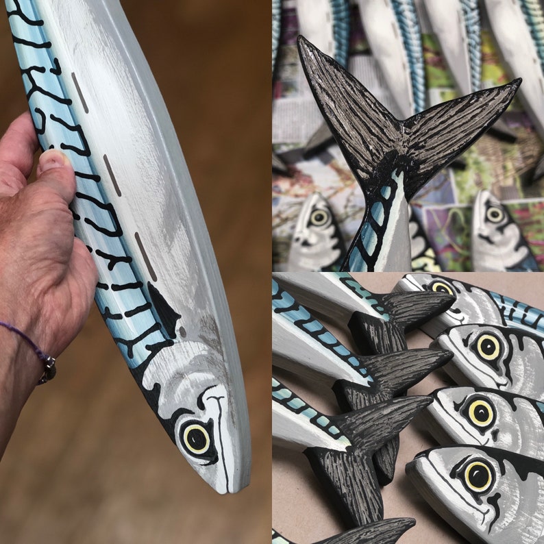 May include: Hand-painted wooden mackerel fish sculpture. The fish is primarily gray with blue and black accents, featuring a detailed eye and tail. The image shows a close-up of the fish and a collection of similar sculptures.