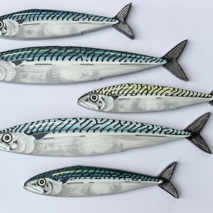 May include: Five mackerel fish decorations with detailed painted scales and fins. The fish are primarily silver with blue and black stripes, and yellow accents. The fish are arranged on a white background.