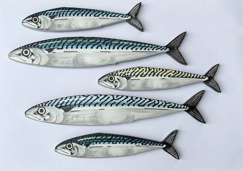 May include: Five mackerel fish decorations with detailed painted scales and fins. The fish are primarily silver with blue and black stripes, and yellow accents. The fish are arranged on a white background.