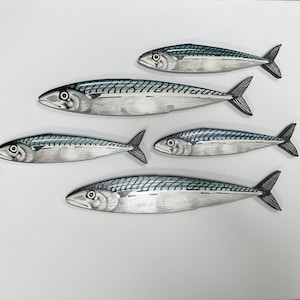 May include: Five mackerel fish illustrations with detailed scales and fins. The fish are primarily silver with blue-green markings along their backs. The artwork is set against a plain white background, creating a clean and simple aesthetic.