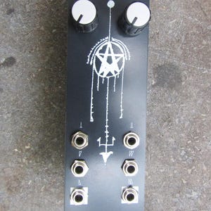 May include: Black electronic device with white graphics and text. Features two white knobs at the top, a pentagram design, and several input jacks. The text "NERIUM" and "REVERSELANDFILL" are visible.