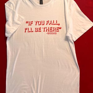 May include: White t-shirt with red text that reads "If you fall, I'll be there" - Ground.