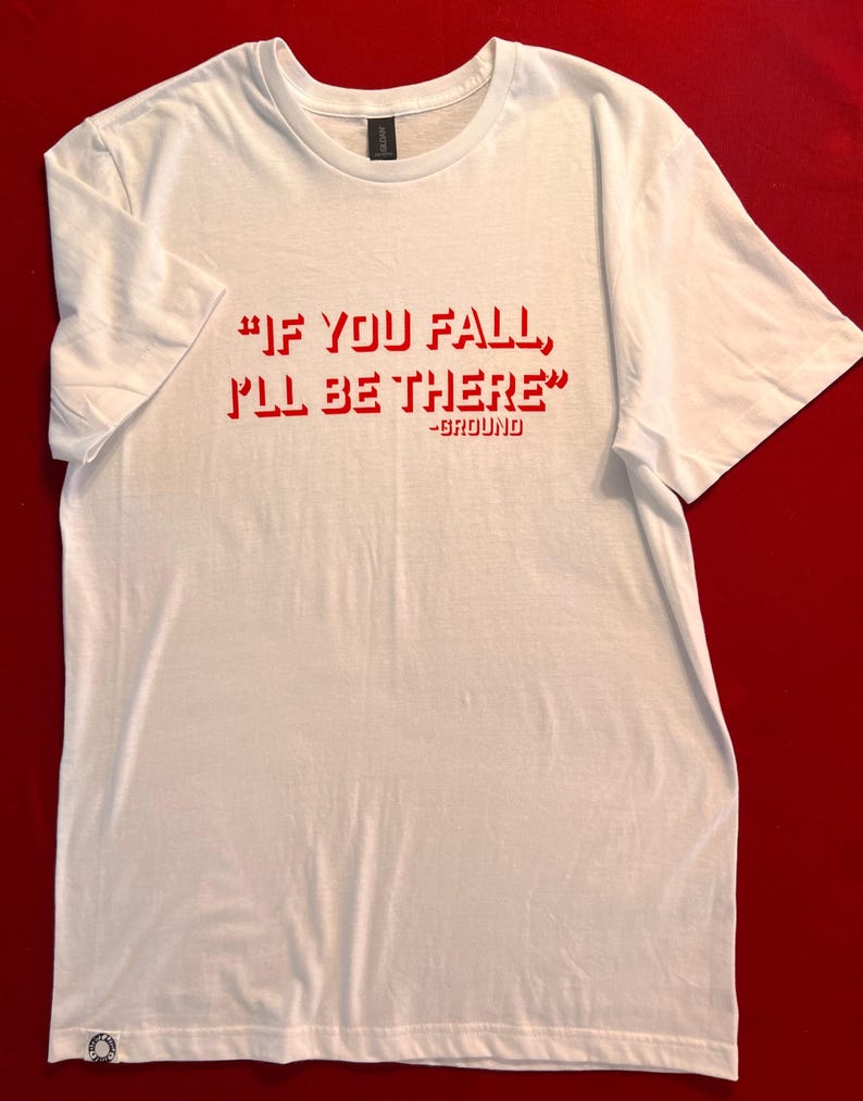 May include: White t-shirt with red text that reads "If you fall, I'll be there" - Ground.