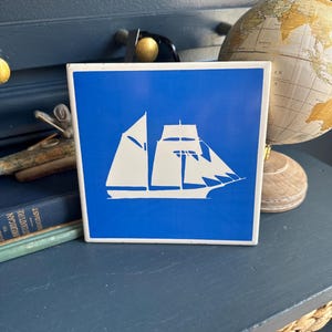 Nautical schooner with royal blue background and white image. Graphic tile can be hung or used as a trivit.