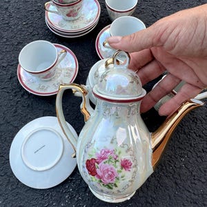 May include: A vintage tea set featuring a pearlescent teapot with gold accents and a floral design. The set includes matching teacups and saucers with a red trim and floral pattern. A classic tea party set.