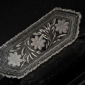 May include: A clear, rectangular glass dish with a floral design. The dish features three etched flowers and leaf patterns. The edges are scalloped, and the dish is likely used for serving or display.