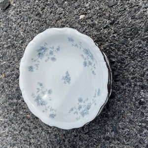 May include: A set of white ceramic bowls with a blue floral pattern. The bowls have a scalloped edge and are stacked on top of each other.