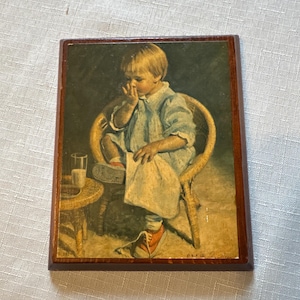 May include: A vintage rectangular wooden plaque featuring a painted image of a young child in a light blue outfit, seated in a wicker chair. The child is touching their face, with a small table holding a glass of milk nearby. The artwork has a warm, nostalgic feel.