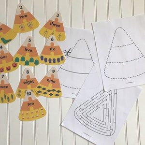 Peut inclure: Un ensemble de dix cartes en forme de maïs sucré orange et jaune avec les chiffres de 1 à 10 et le mot correspondant pour chaque chiffre. Les cartes sont conçues avec des images sur le thème d'Halloween. Il y a aussi deux feuilles imprimables en noir et blanc, l'une avec un contour de maïs sucré et l'autre avec un labyrinthe de maïs sucré.