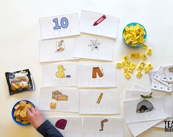 May include: A set of printable flashcards with pictures of various objects, such as a spider web, a crayon, and a dog. The cards have blank spaces for children to write the corresponding words. There are also letter tiles and a bag of alphabet crackers.