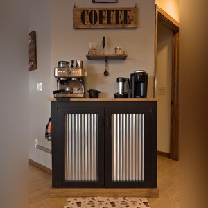 Farmhouse Coffee Bar Cabinet painted black with corrugated metal doors, in a home coffee station under a wood COFFEE sign and a small wall shelf